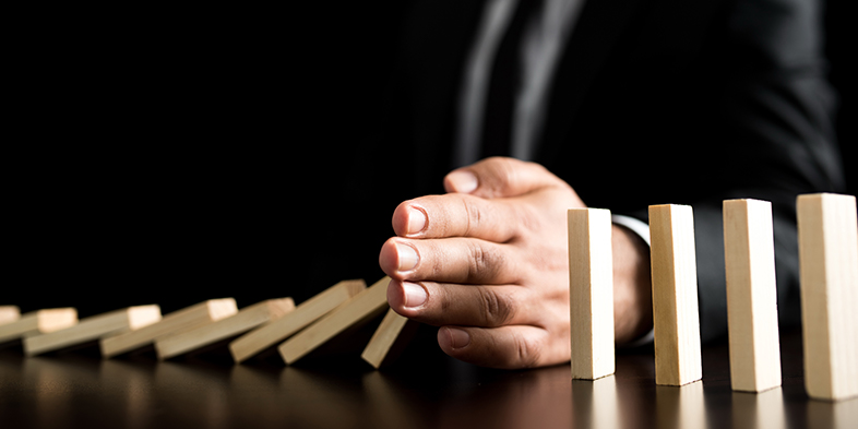 Businessman preventing Dominoes Chain from toppling
