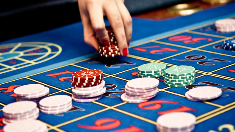 Blue casino roulette table and female hand holding gambling chips