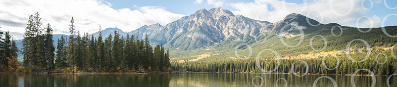 Wide angle view of calm lake, green trees, and mountains.